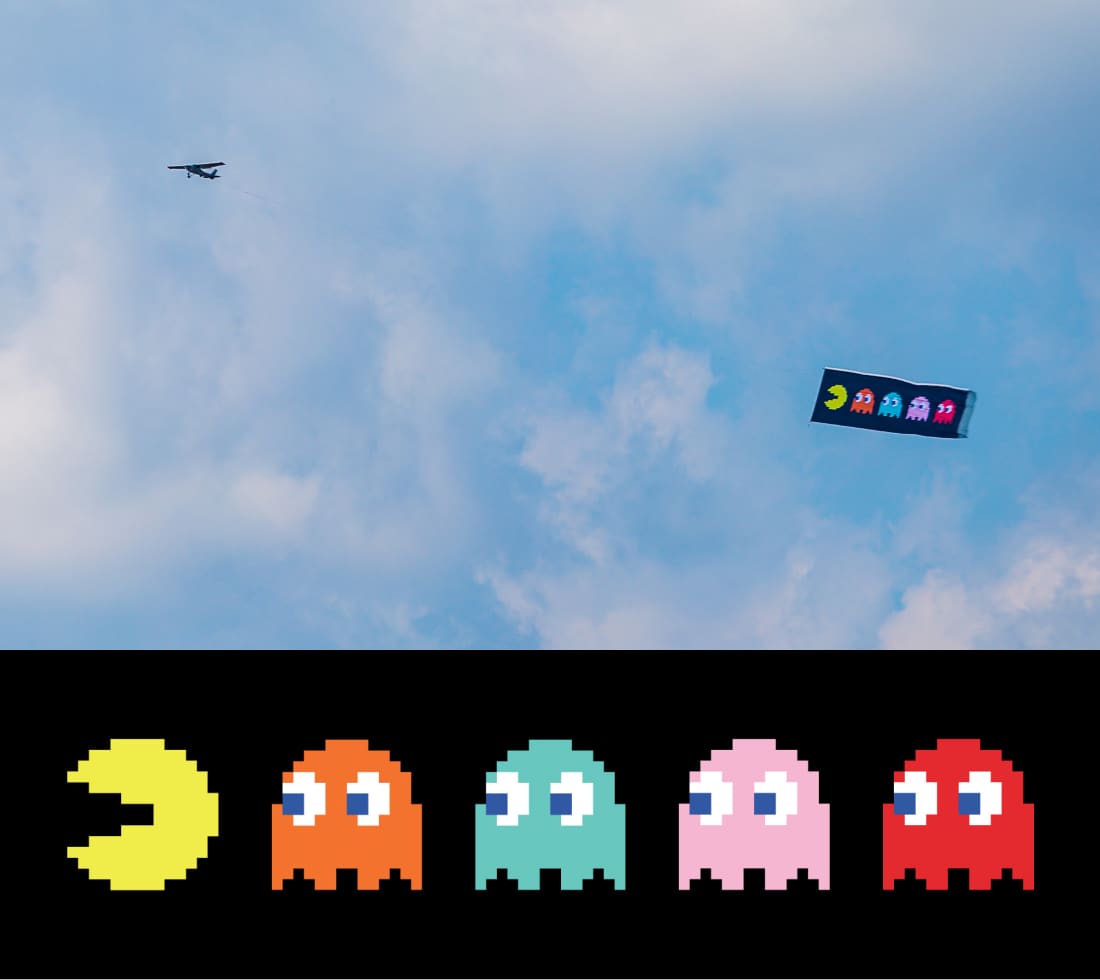 Photograph of plane flying a banner showing four ghosts chasing Pac-Man.