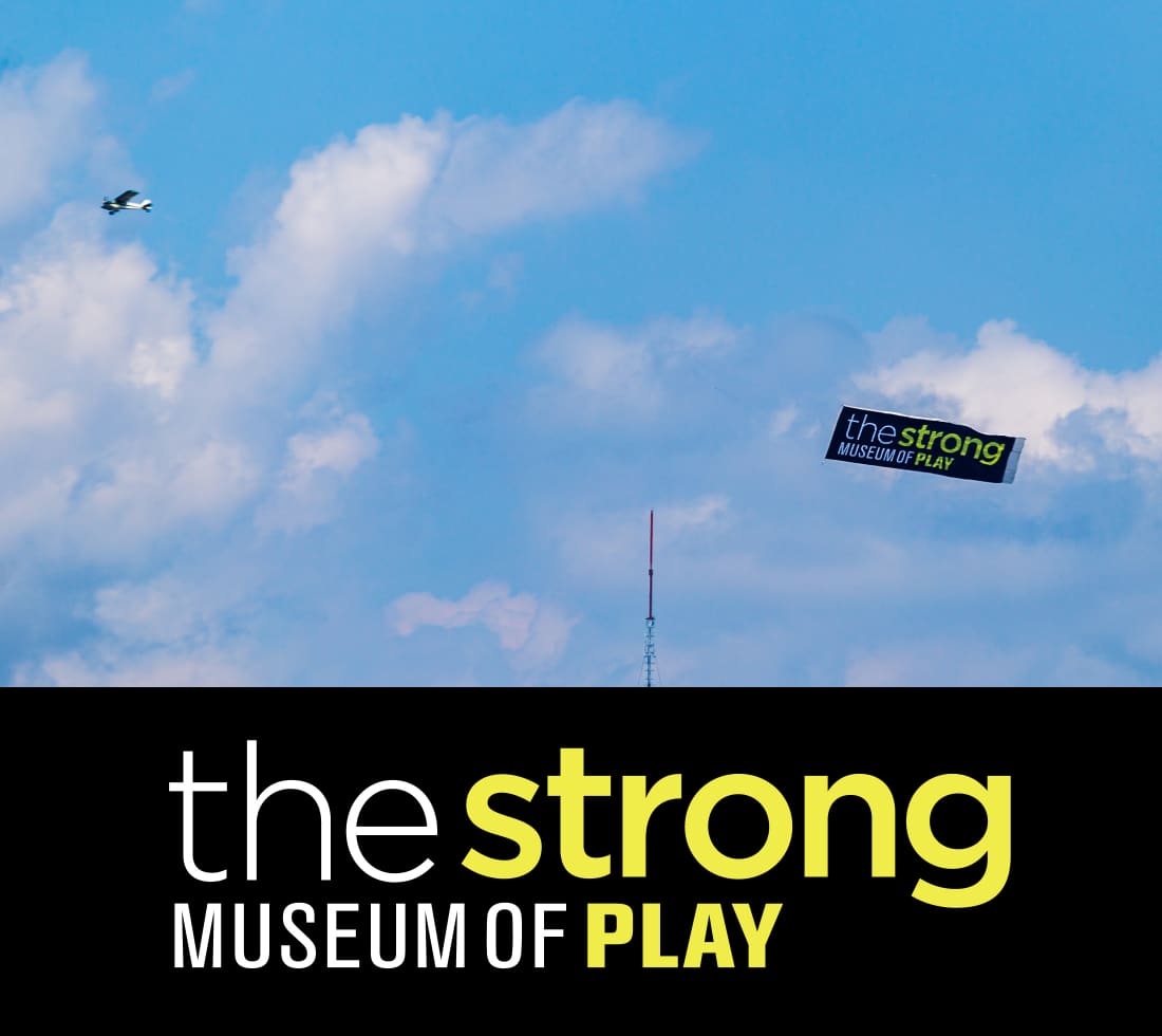Photograph of a plan flying a banner with The Strong National Museum of Play logo.
