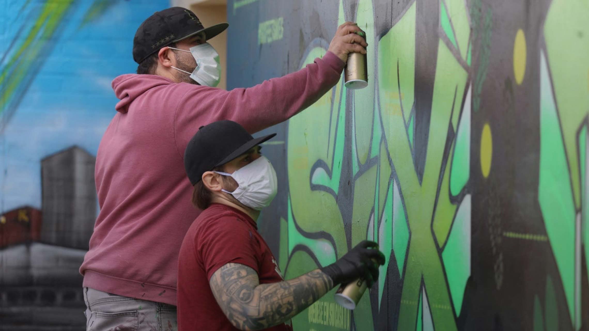 Photograph of two men spraypainting graffiti on a wall.