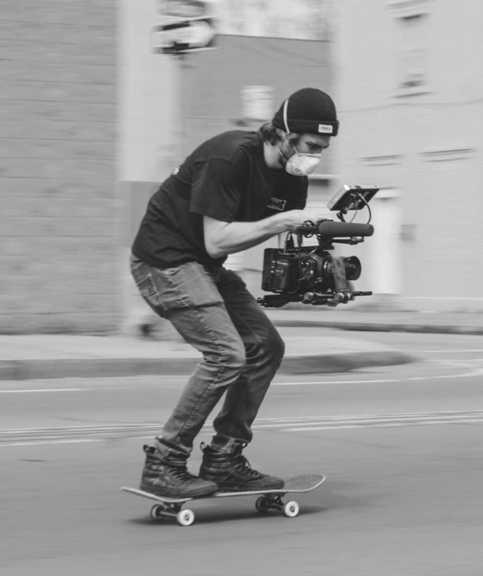 Photograph of someone filming while on a skateboard.